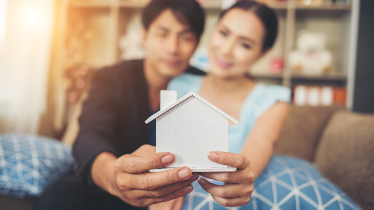 Young couple holding a white miniature house in living room